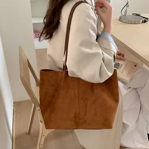 Close-up of a brown suede tote bag with slim leather straps worn with a beige trench coat