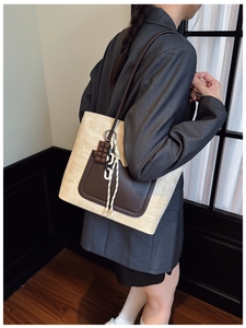 Detail of woven straw tote bag with brown leather pocket shown on a gray suit model