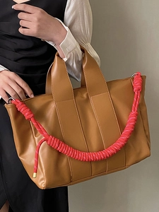 Large caramel leather tote bag with unique red braided shoulder strap for daily commuting