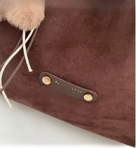 Close-up of brown suede tote bag with leather strap, gold rivets and a soft pink pompom