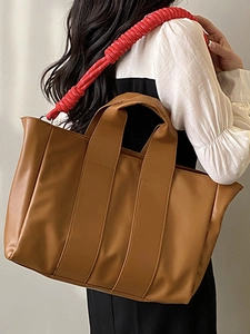 Brown tote bag with distinctive red spiral shoulder strap for commuting and travel