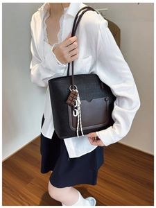 Detail of black woven tote bag with brown leather pocket and cute charm accessory