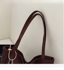 Detail of dark brown suede tote bag with reinforced handles and beaded chain accent