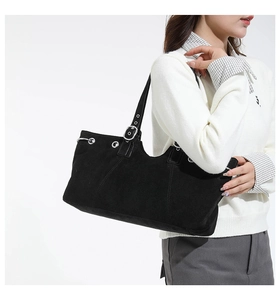 Detail of black suede tote bag with silver eyelets and adjustable strap on a model