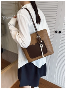 Detail showing woven brown tote bag with leather pocket and chocolate charm accessory