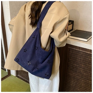Détail du sac cabas en daim bleu marine avec motifs fleuris porté sur un trench-coat beige