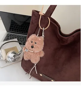 Detailed view of a brown plush dog charm with a pearl necklace on a leather tote bag