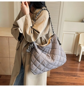 Detail view of grey quilted tote bag with black and white striped woven shoulder strap