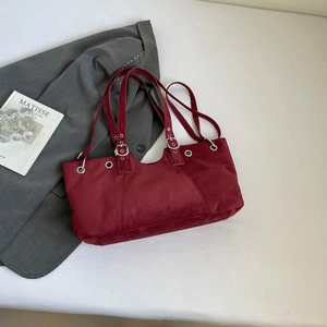 Close-up of deep red suede tote bag with silver eyelets on a gray suit jacket