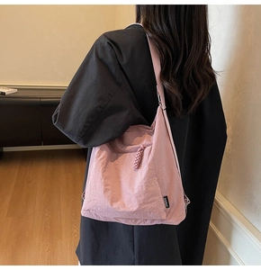 Détail du sac bandoulière en nylon rose montrant la fermeture tressée et l'étiquette