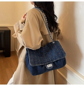 Detail of a large denim shoulder bag with silver quilted stitching and metal chain strap