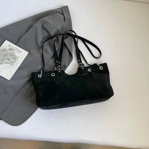 Detail of black suede tote bag with silver eyelets and adjustable straps on a grey blazer