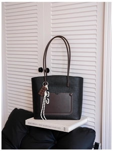 Detail of black woven tote bag featuring brown leather front pocket and chocolate charm