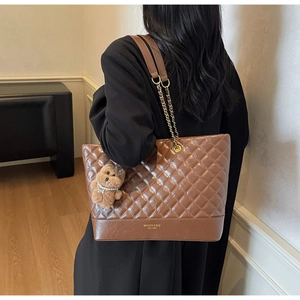 Detail view of large brown quilted tote bag featuring gold chain strap and teddy bear charm
