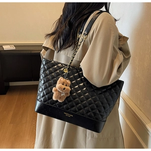 Detail of black quilted tote bag with gold chain strap and cute brown plush bear charm