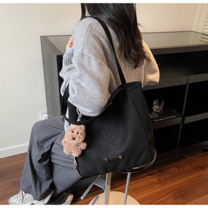 Detail of black suede tote bag with brown logo plate and cute plush bear accessory