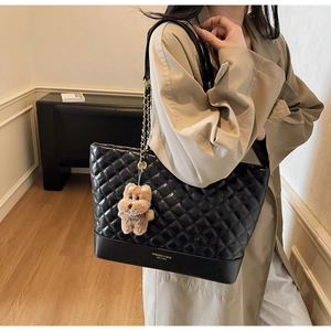 Detail of black quilted tote bag with gold chain strap and brown plush bear charm