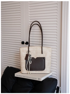 Close-up of woven straw tote bag with brown leather pocket and decorative charms