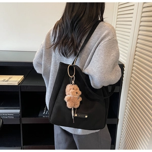 Close-up of black canvas tote bag with leather logo tag and cute brown teddy bear charm