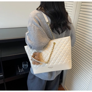 Detail view of cream quilted tote bag with gold chain strap and cute bear charm pendant