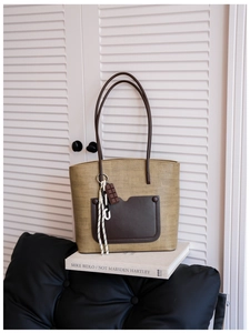 Detail view of woven straw tote bag with brown leather handles and decorative chocolate charm
