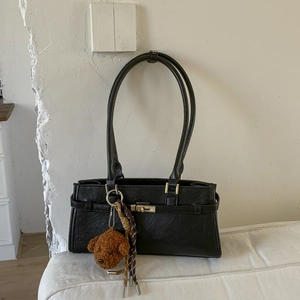 Detail view of retro black leather shoulder bag featuring metal buckle and teddy bear charm