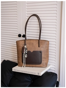 Retro brown woven tote bag with leather pocket and decorative charm on white books