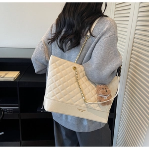 Detail shot of beige quilted tote bag with chain strap and cute bear plush pendant