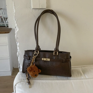 Detail shot of vintage brown underarm bag with gold metal clasp and plush bear charm