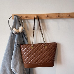 Close-up of brown quilted tote bag featuring a gold logo and leather chain shoulder strap
