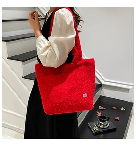 Detail view of large red plush tote bag with wide shoulder strap and silver logo
