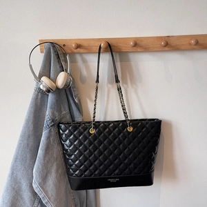 Detail of the black quilted tote bag hanging with chain strap and brand logo