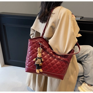 Detail of burgundy quilted tote bag with rabbit pendant and fashion text on beige coat