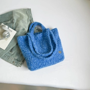 Detail of blue plush tote bag with soft faux fur texture and a small metal heart