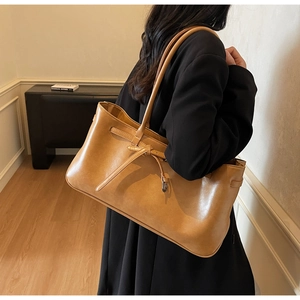 Detail of a brown leather tote bag with a decorative knotted strap and shoulder design