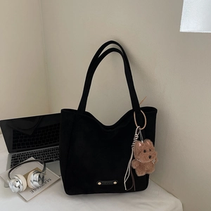 Détail d'un sac cabas en daim noir avec breloque ours en peluche et logo en métal
