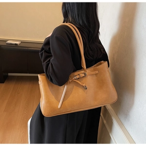 Detail view of large caramel brown faux leather tote bag with decorative strap being worn
