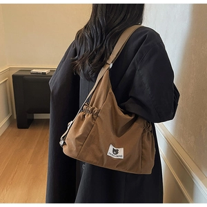 Detail of brown canvas shoulder bag with branded logo patch and metal strap buckle