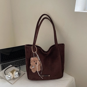 Détail d'un sac cabas en daim marron foncé avec un pendentif d'ours en peluche doux