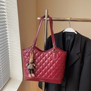 Detail of burgundy quilted tote bag featuring a cute bunny plush charm on a display stand