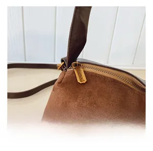 Détail de la fermeture éclair dorée sur le sac baguette en daim marron avec texture macro