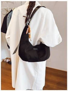Detail of black suede hobo bag with ethnic wooden bead charm and minimalist logo patch