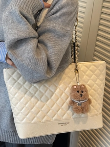Beige quilted tote bag with gold chain strap and cute bear charm shown on model