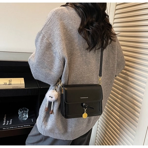 Close-up of minimalist black leather crossbody bag with knot decor and plush pendant