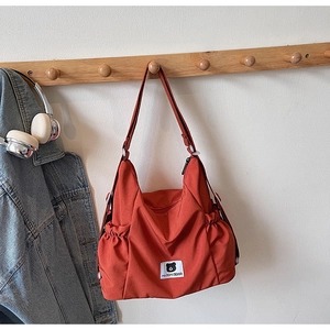 Detail view of brick red nylon tote bag with bear patch and drawstring side pockets