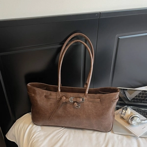 Detail of a vintage dark brown tote bag with metal buckles on a white fabric surface