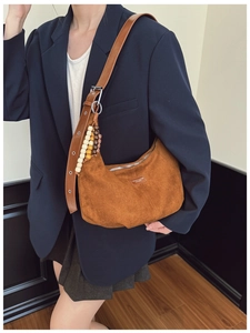 Detail of brown suede crescent bag with adjustable leather strap and beaded charm
