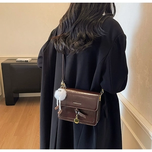 Detail of dark brown vintage leather crossbody bag with pompom charm and gold lettering