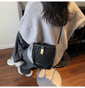 Detail of black leopard embossed bucket bag with gold metal buckle on female model