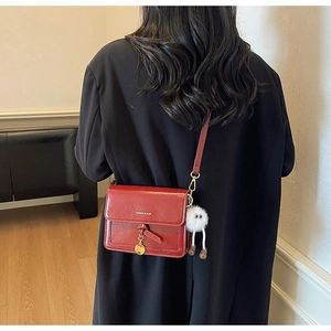 Detail of red patent leather crossbody bag featuring fashion text and cute plush pendant